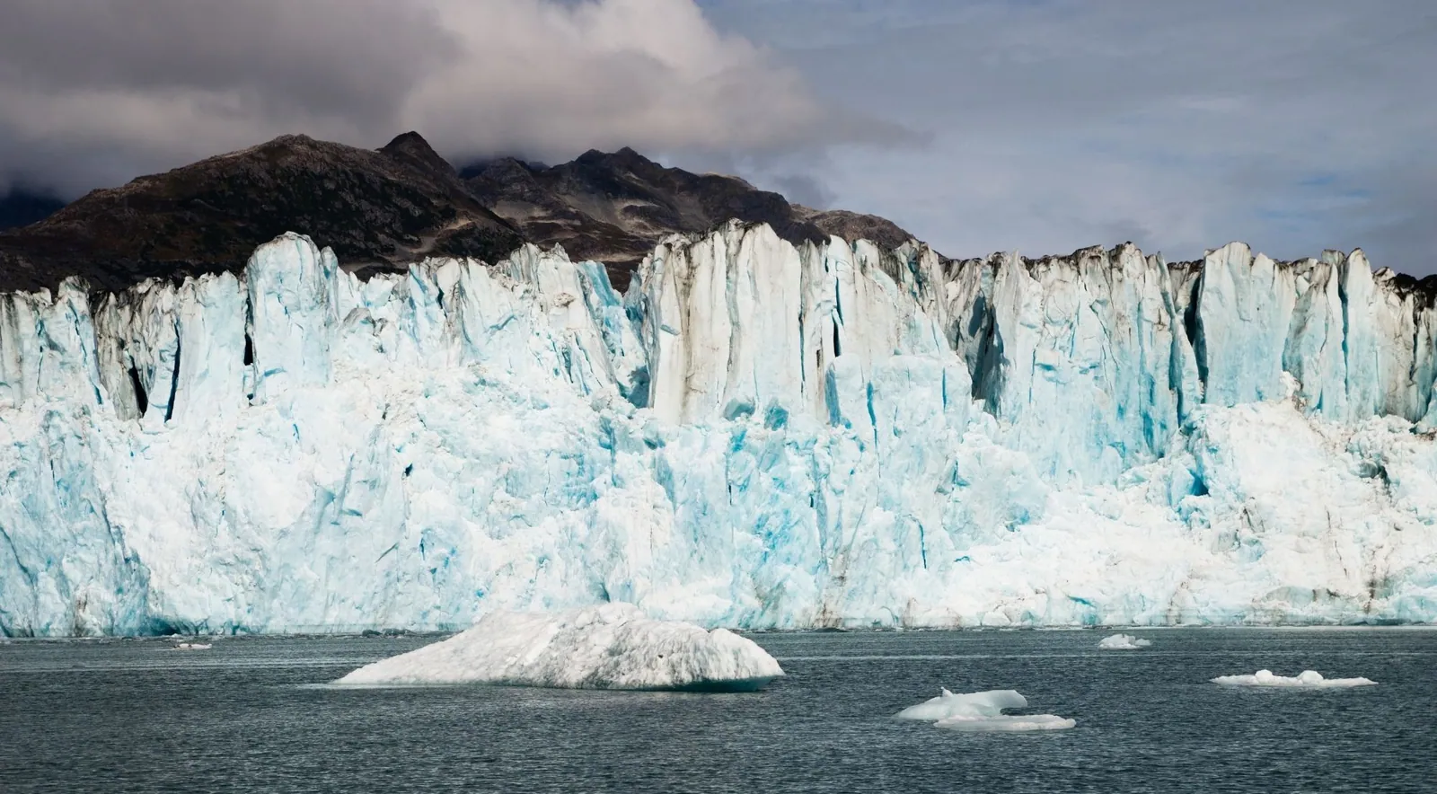 A wide wall of blue tidewater glacier ice calving into the sea in Aialik Bay