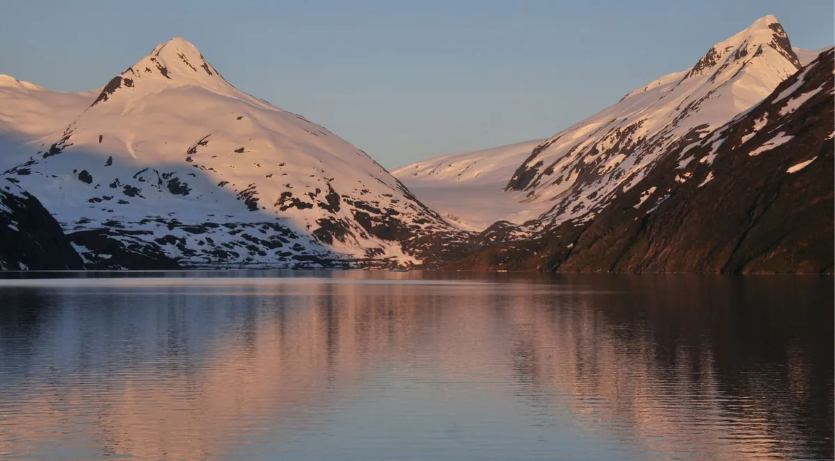 Snowy peaks glowing pink at sunset above a calm fjord