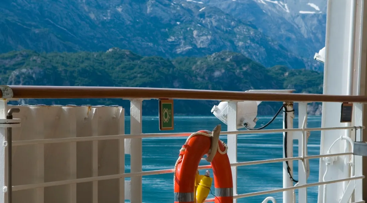 View from a tour boat deck across a fjord toward forested mountains
