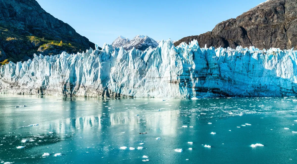 Sunlit tidewater glacier shedding icebergs into turquoise water